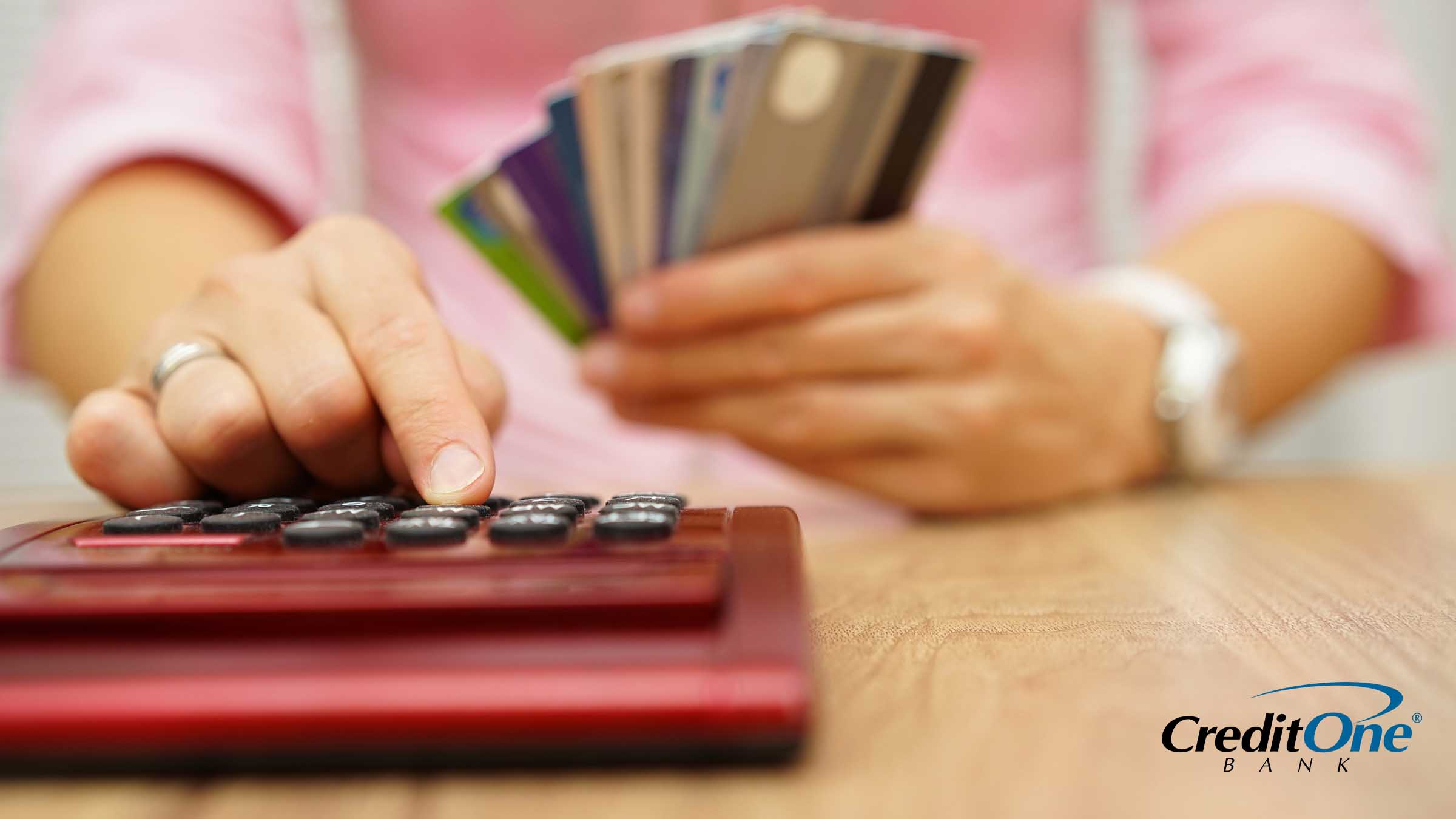 A woman’s hand uses a calculator as her other hand holds a pile of fanned-out credit cards, perhaps as she calculates the value of her credit card annual fees.